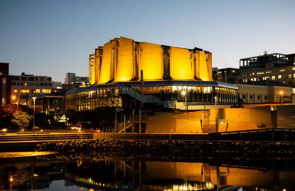 Michael Fowler Centre lit up at dusk with Whairepo Lagoon in the foreground