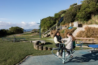 Two girls playing on a spinning piece of equipment in a playground.