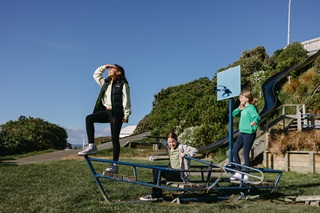 Three girls standing and sitting on top of a piece of playground equipment.