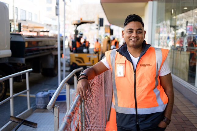 Transport and Infrastructure Manager Brad Singh, wearing a high-vis and smiling, with his arm casually leaning on the fencing of a worksite.