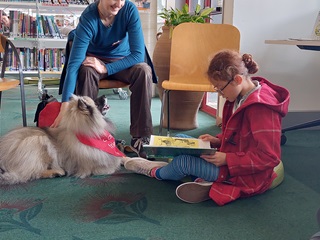 Read to Kurī programme at the library . A young girl reading next to a dog. 