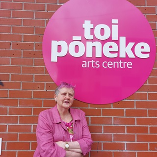 Woman standing infront of a brick wall with a pink jacket on.