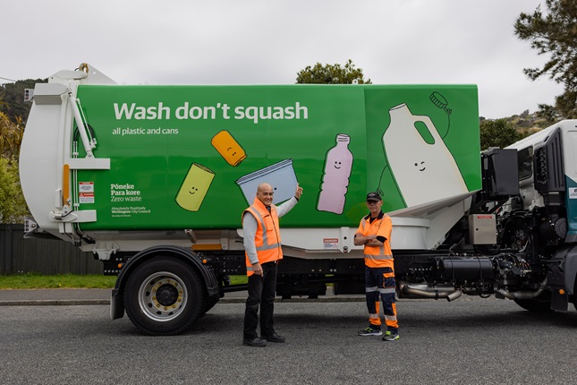 Two people wearing high vis jackets standing infront of a recycling truck.