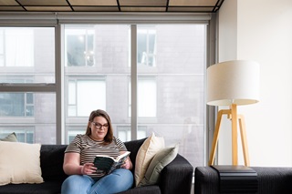 Woman wearing a striped tshirt sitting on the couch reading a book.