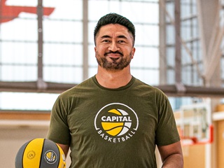 Man wearing a green tshirt holding a basketball inside a gym.