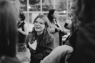 A black and white image of a woman smiling and holding a glass of wine.