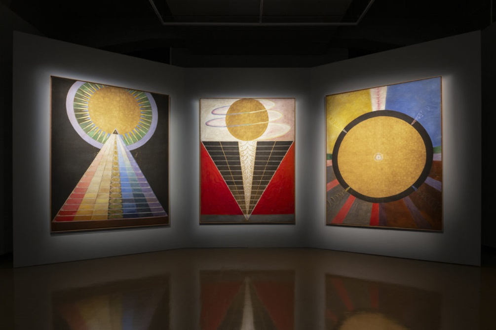 Three large paintings by Hilma Af Klint with golden spheres and rainbows.