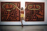 A drag queen posing in front of two large red and black Keith Haring paintings at the opening of his exhibition at City Gallery Wellington.