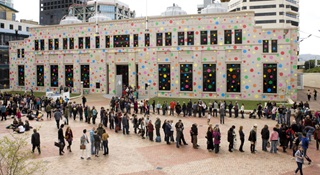 A long line of people queing to get into City Gallery Wellington which is covered in large colourful dots.