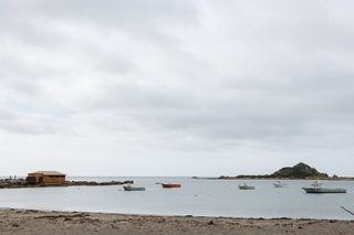 A beach and ocean with boats surrounding a small island in the background.