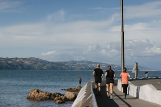 People running on the side of the road with the harbour in the background.