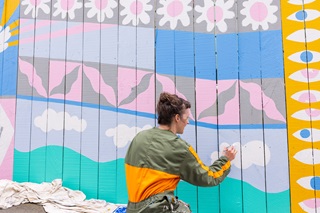Person painting a mural on a fence.