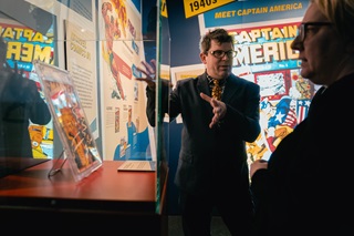 Marvel curator standing infront of a case and speaking.