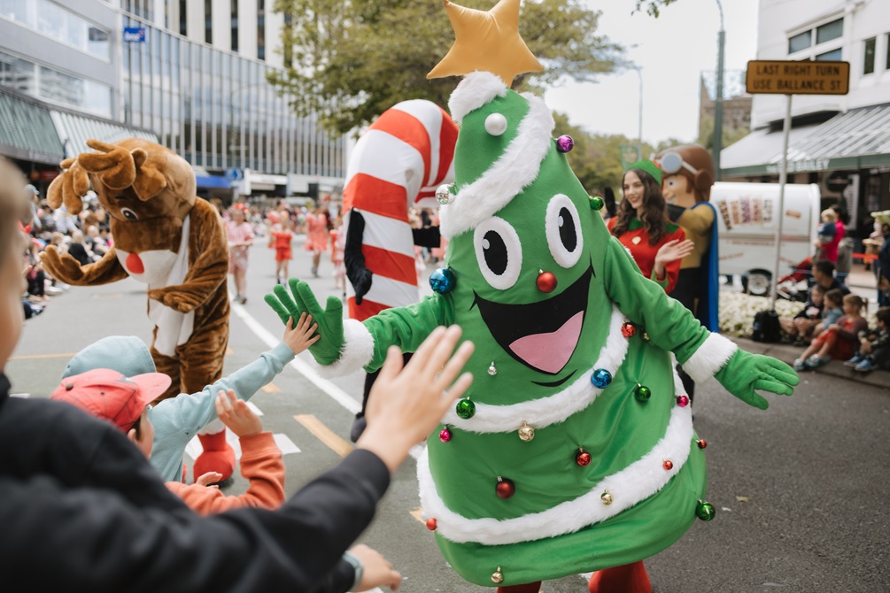 A performer dressed as a Christmas tree with a big smiley face and a gold star on their head high fives children attending A very Welly Christmas 2022.