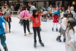 A child on ice skate in the ice rink with arms spread wide.