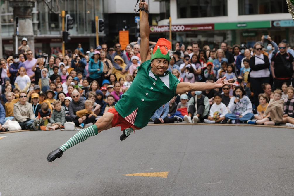 A performer dressed as a Christmas elf performs for crowds.