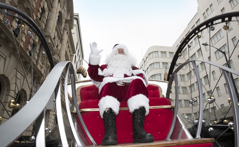 A performer dressed as Santa Claus riding a carriage float, viewed from a low angle.