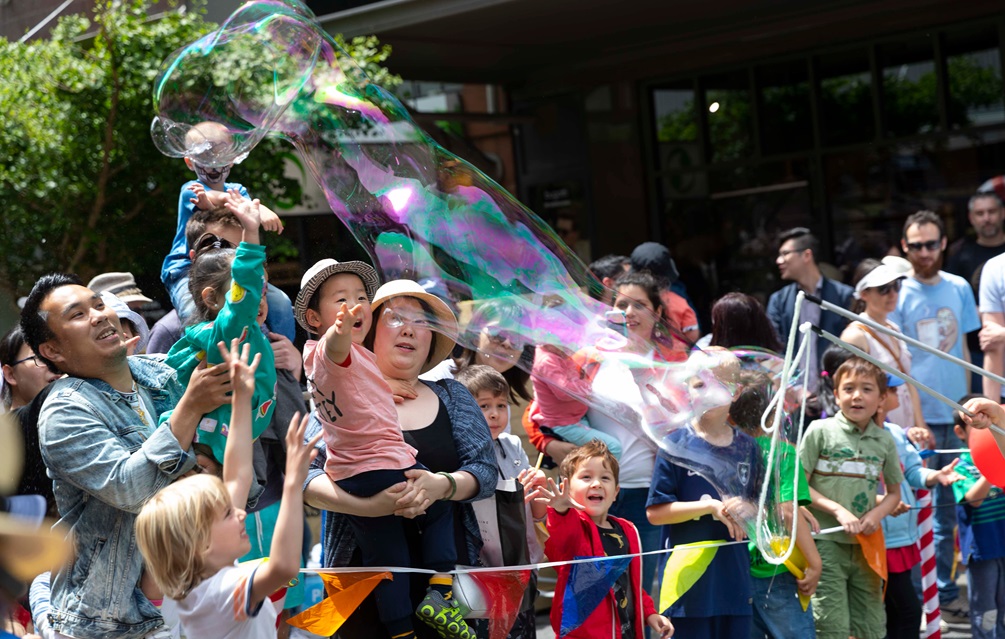 A performer blowing giant bubbles, with a crowd watching on in the background.
