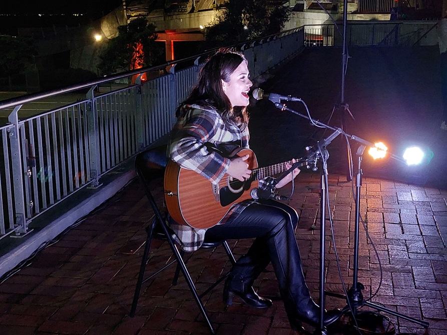 Women playing the guitar at Civic Square at nighttime.
