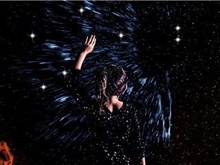 Girl facing stars and reaching up.
