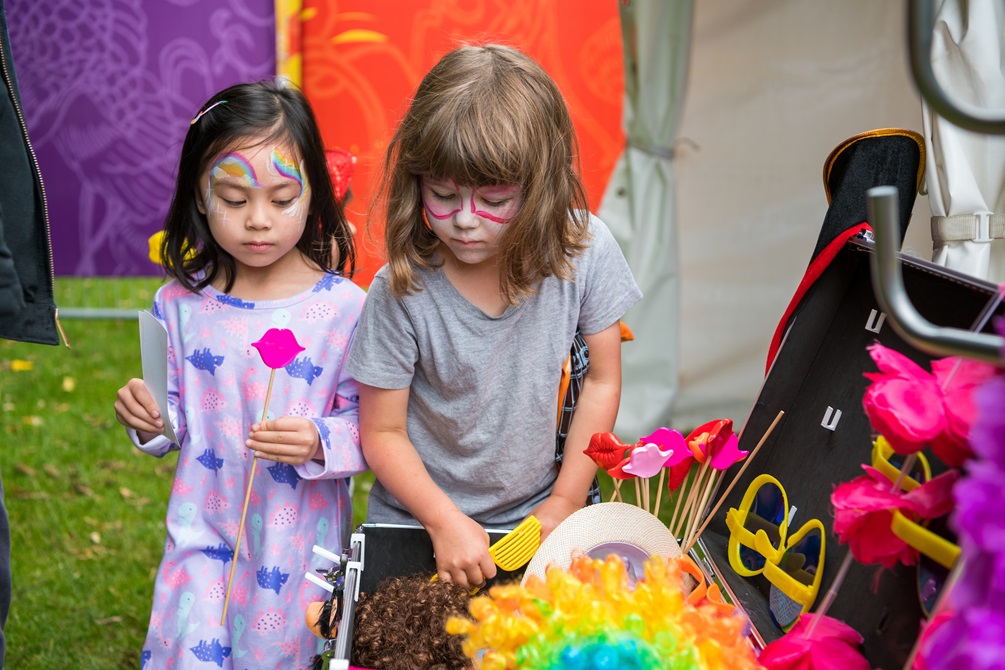 Two children with painted faces search through costume accessories.