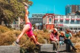A performer doing the splits on the waterfront while a family looks on.