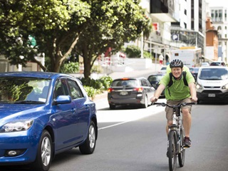 Man in green shirt cycling next to a blue Mazda.