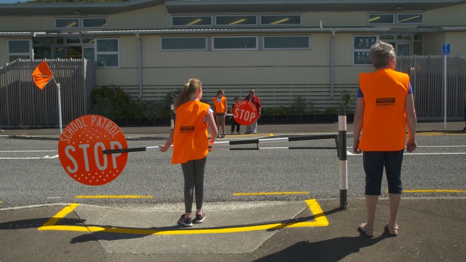 An adult and two children wearing high vis vests and holding the school pedestrian crossing signs on a road.