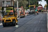 Workers and machinery surfacing a road with asphalt. A steam roller is smoothing the surface.