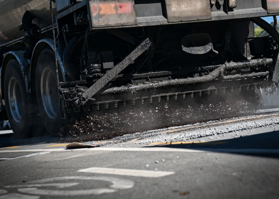 A truck with spray attachment dropping a layer of hot bitumen on a road.