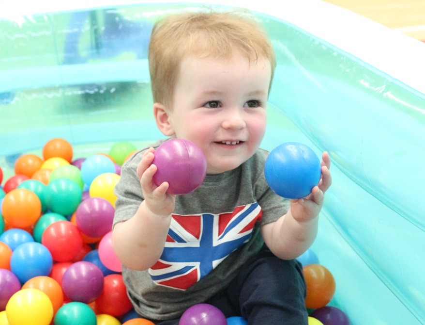 Toddler sitting in a blow-up pen surrounded by coloured balls.