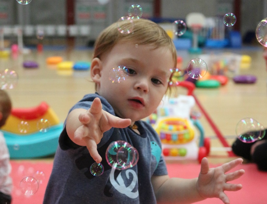 Toddler reaching out towards some bubbles that are floating in the air.