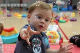 Toddler reaching out towards some bubbles that are floating in the air.