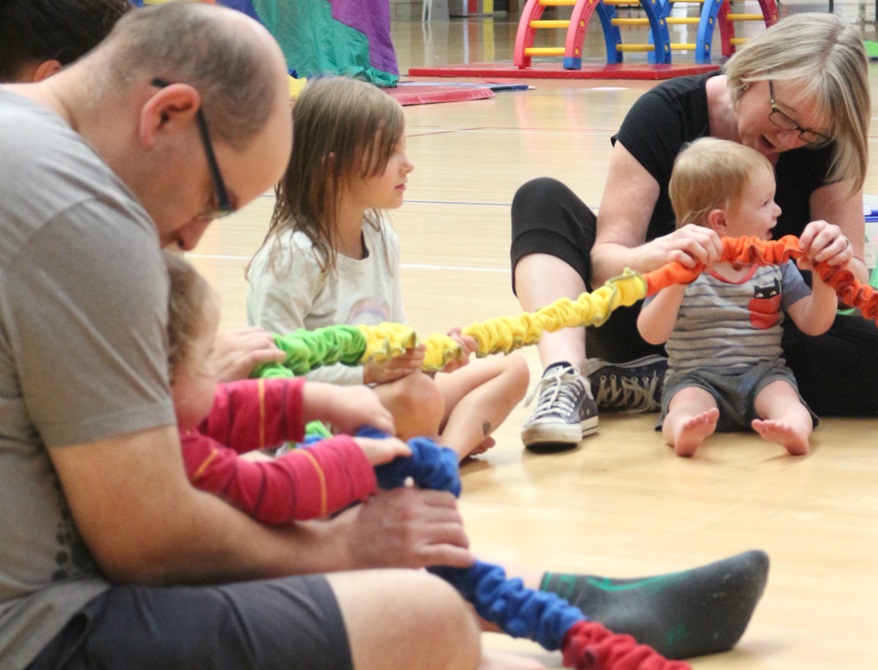 Children and adults sitting in a circle holding a coloured rope.