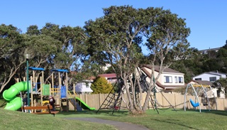 Play area with a fort, bright green tube slide, climbing frame, swings.