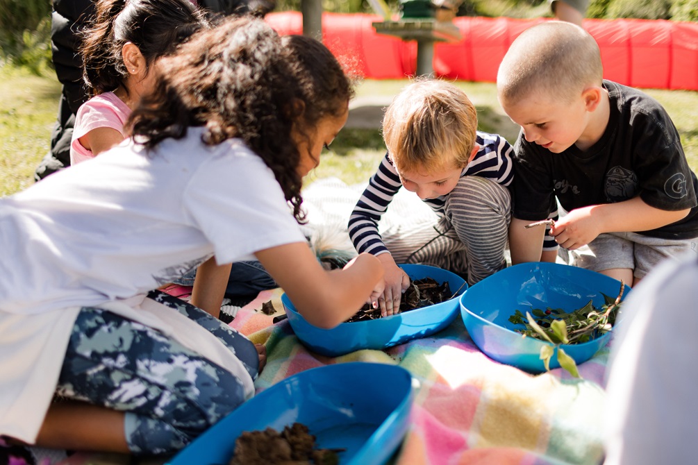 Children sorting through collected leaves and foliage in plastic containers.