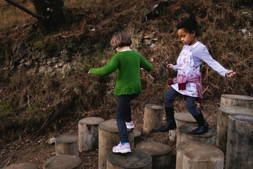 Two children stepping down a slope on wood blocks shaped like tree stumps.