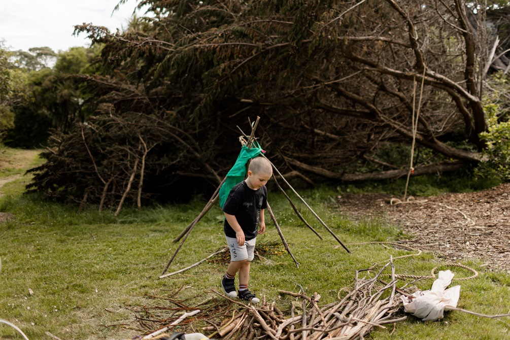 A child constructing a tent-like structure made of long sticks.