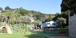 Playground showing a large grass area, swings, a fort with slide and a climbing wall.