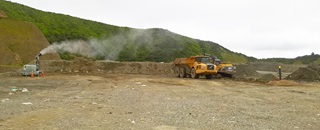 Wellington landfill, showing the large space on a bleak, overcast day. Large yellow trucks and machinery can be seen operating on it.